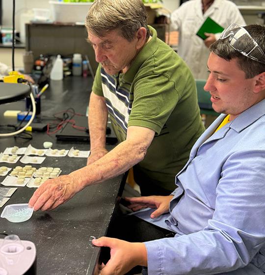 man with lab coat and another man with polo shirt, looking over materials