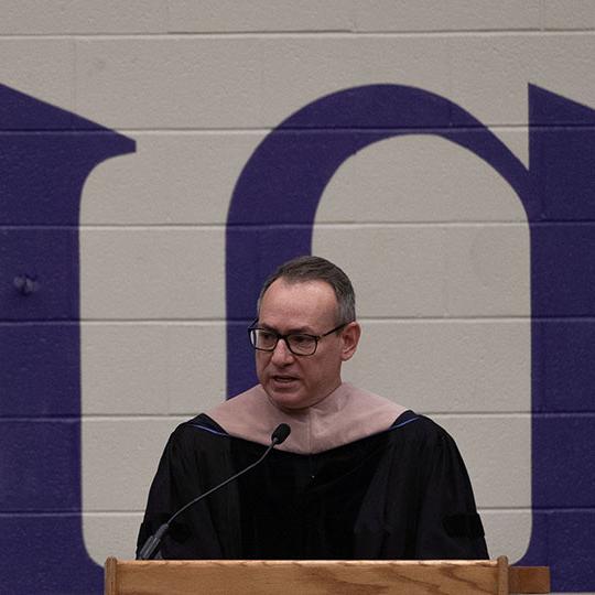 man with glasses and robe speaking at a podium