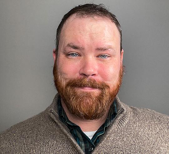 headshot of man with beard wearing sweater and smiling